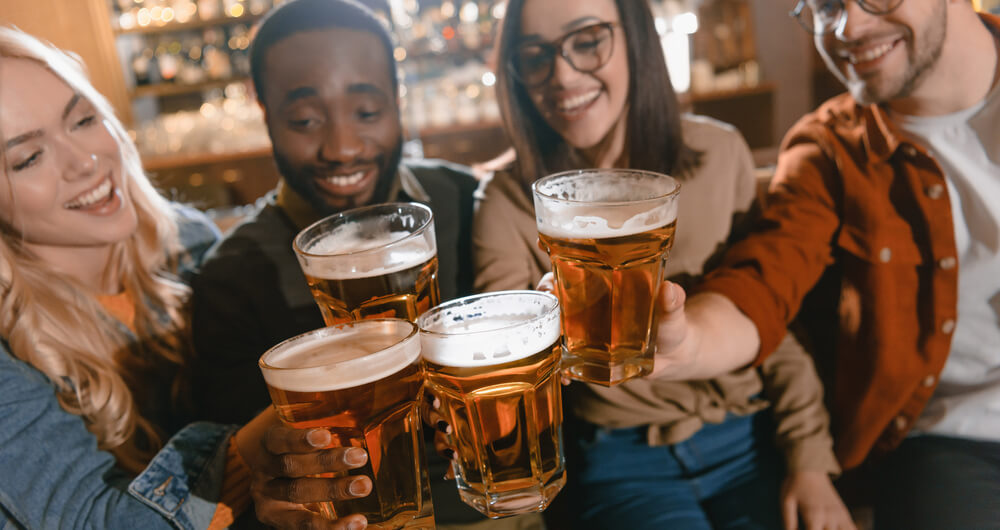 Cheerful friends drinking beer together at bar